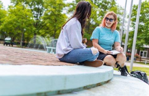 Two female students are sitting on the steps in front of the Webb center talking